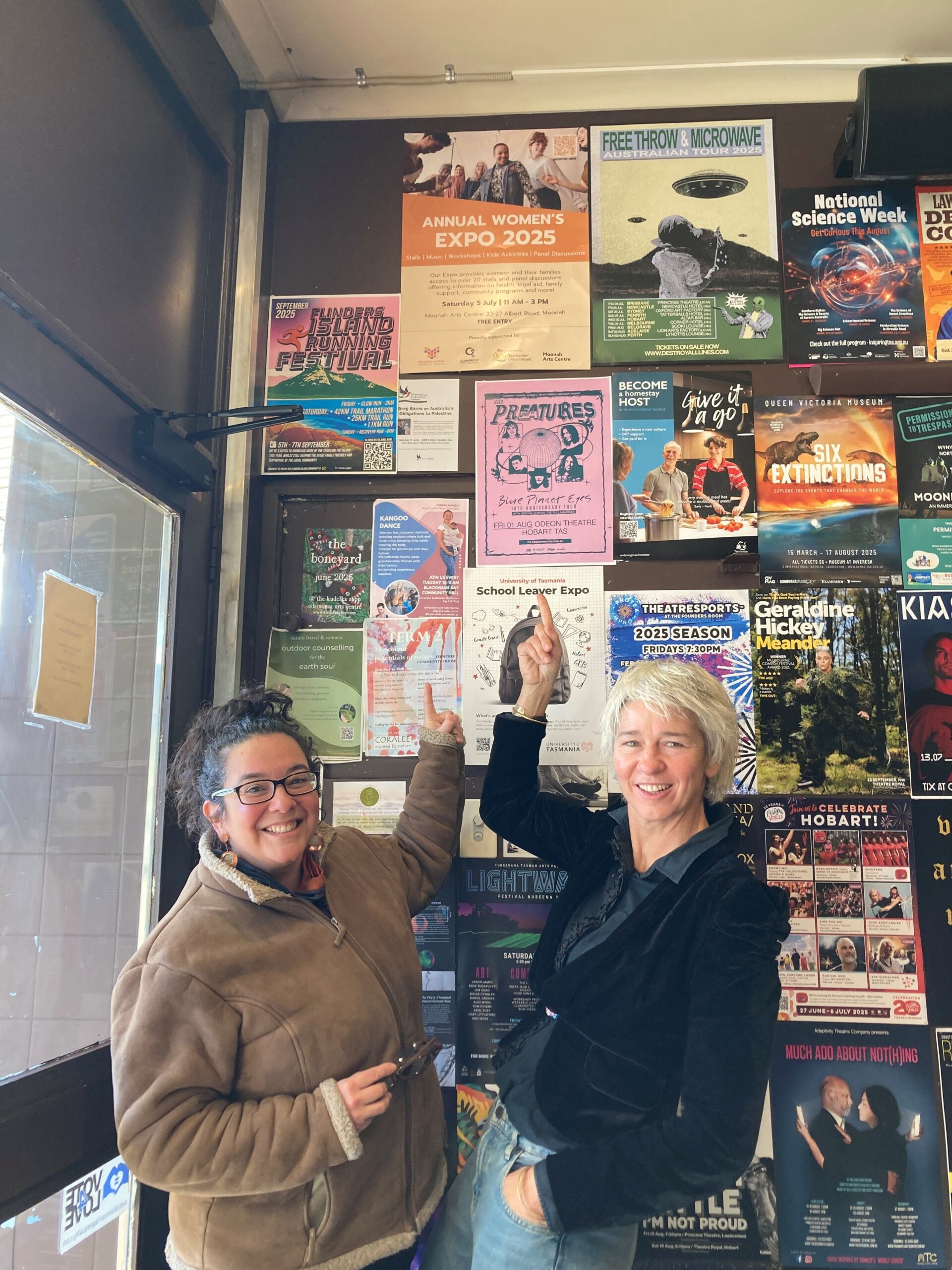 A Fairer World’s Gabrielle Gartrell, and Multicultural Council of Tasmania's Joanna Cubillos pointing at the Women’s EXPO poster at Ginger Brown cafe